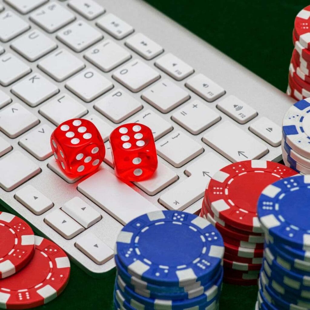 red and blue stacks of poker chips surrounding a computer keyboard with two red six-sided dice on it