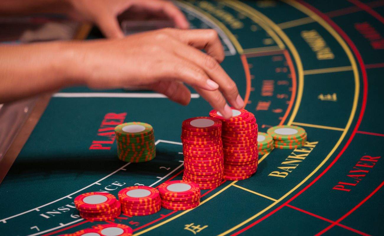a hand of a dealer is organizing the red and green baccarat chips on a baccarat gaming table in a casino
