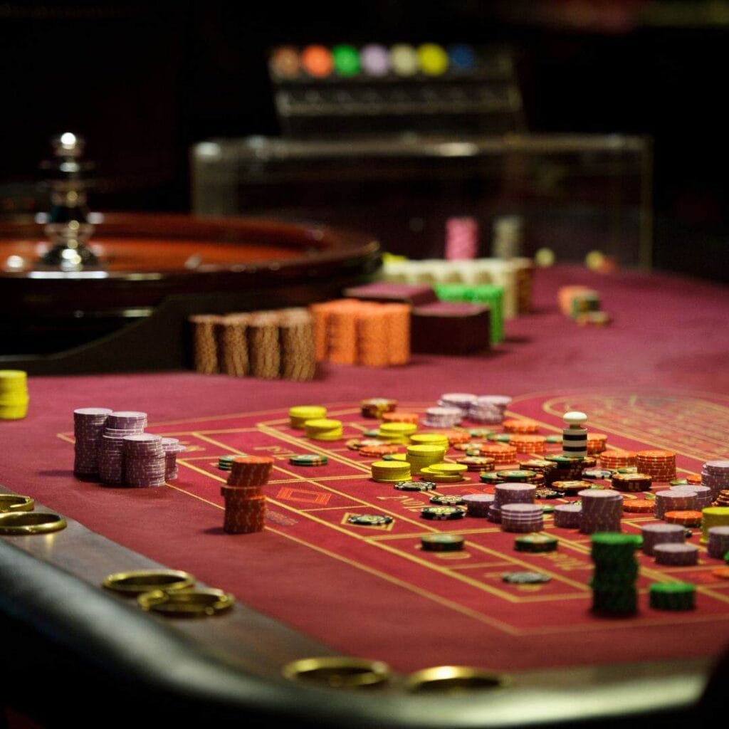 a roulette table with stacks of poker chips placed on it in a casino with the wooden roulette wheel in the background