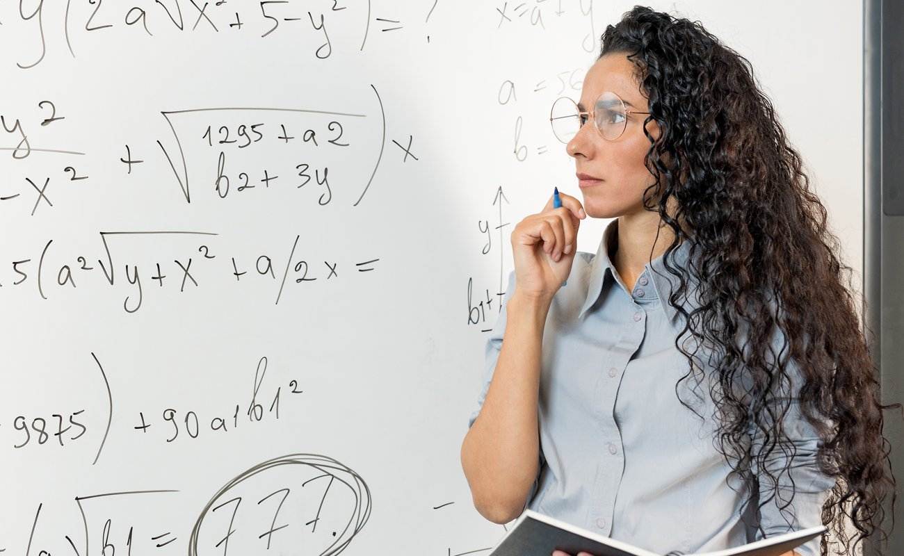 A woman wearing glasses looking at a math formula on a whiteboard.