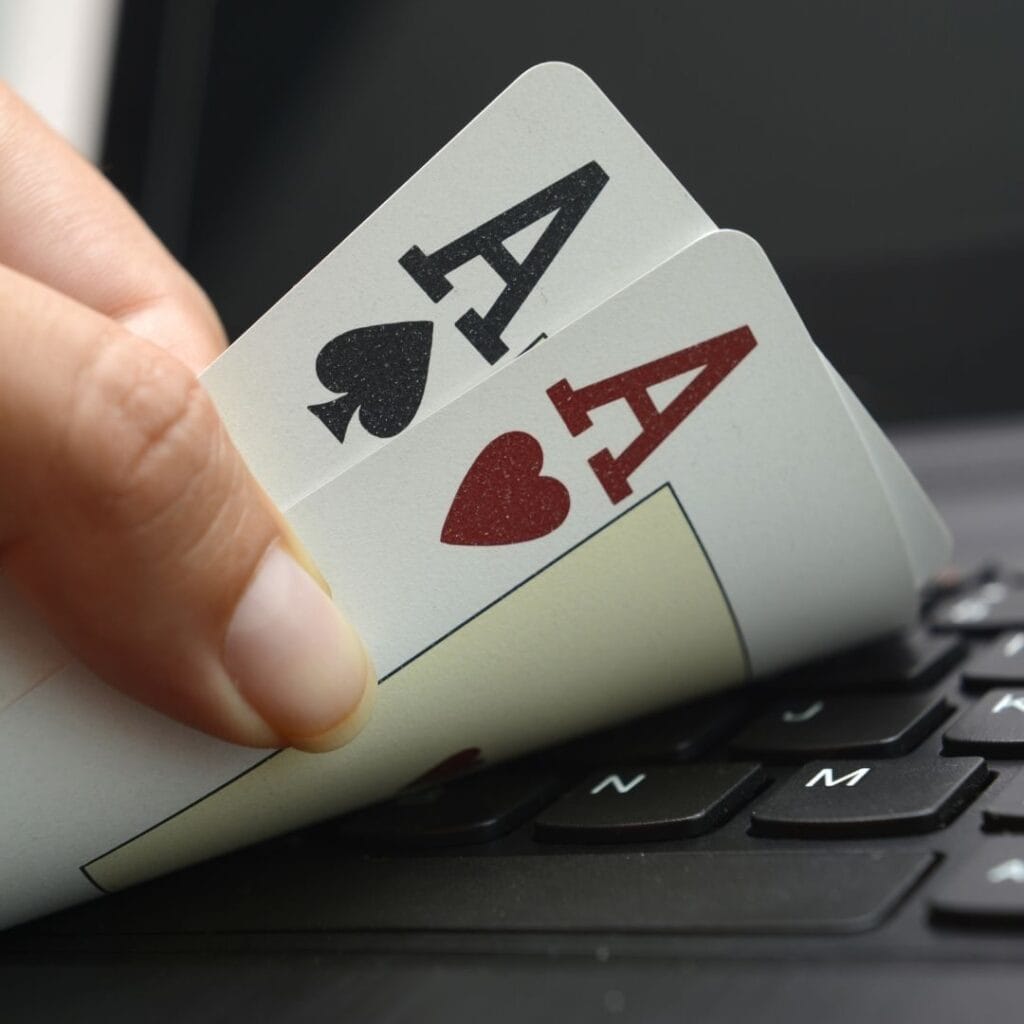 close up of a person lifting a pocket pair of ace playing cards on a computer keyboard to look at them