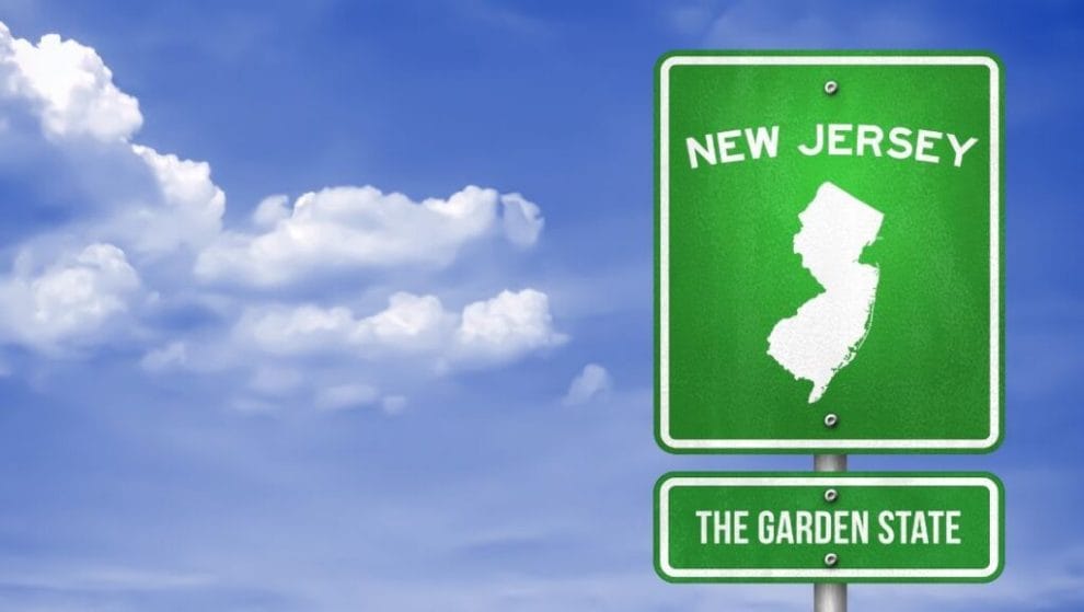 A photograph of a green New Jersey highway sign, with a bright blue sky in the background.