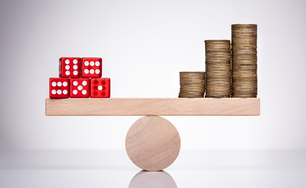  a balancing weight scale with five red six-sided dice on one side and three stacks of coins from shortest to tallest on the other side of the scale 