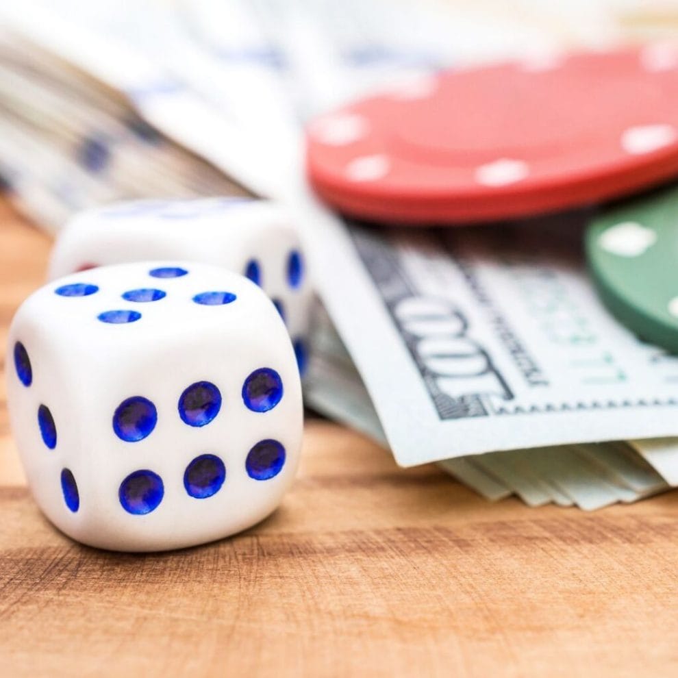 six sided dice in front of money bills with poker chips on them on a wooden surface