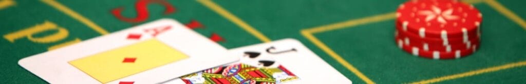 An Ace and Jack of cards laid on a blackjack table, accompanied by a stack of red casino chips.
