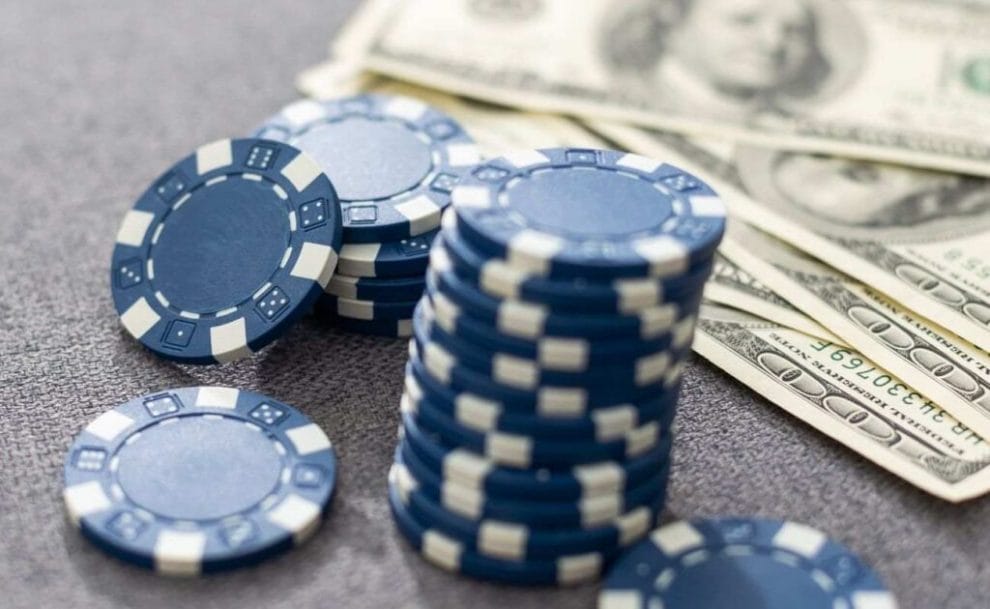 Blue casino chips and money on a grey surface.