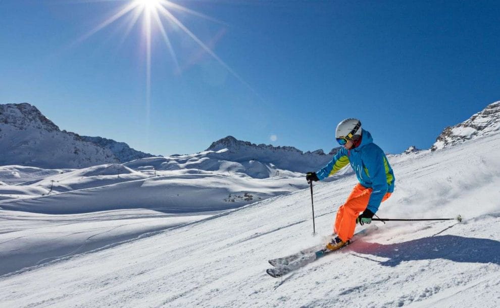 a person in ski gear skiing down a snowy slope with the sun shining in the blue sky