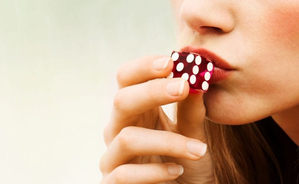 a close up of a woman kissing a red six-sided dice for good luck