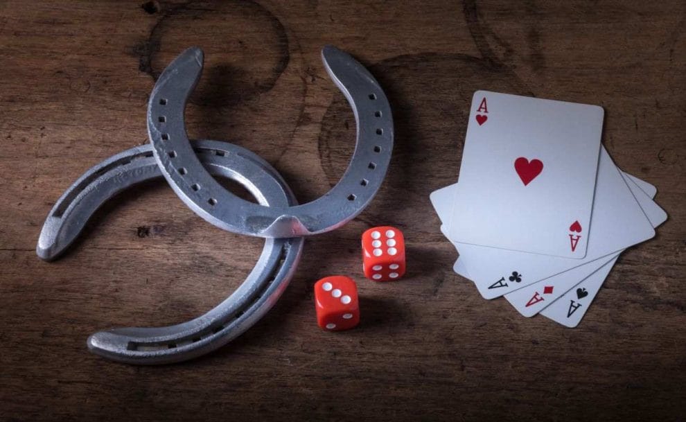  two horseshoes as good luck charms next to a pair of red six-sided dice and four of a kind ace playing cards on a wooden surface 