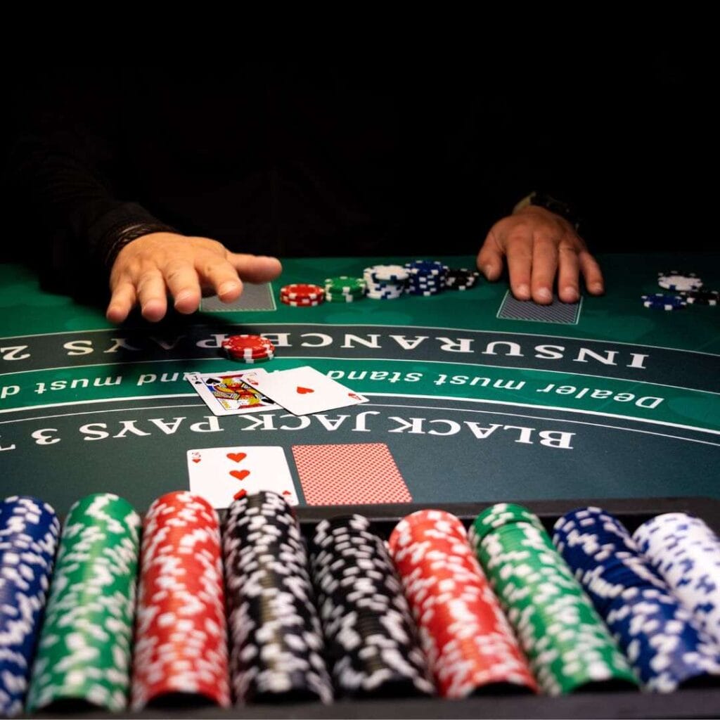 A person seated at a blackjack table, gathering chips with cards laid out before them