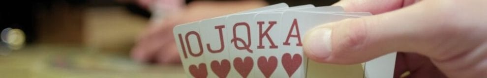 a person checks their poker hand, a royal flush of hearts, during a game of poker