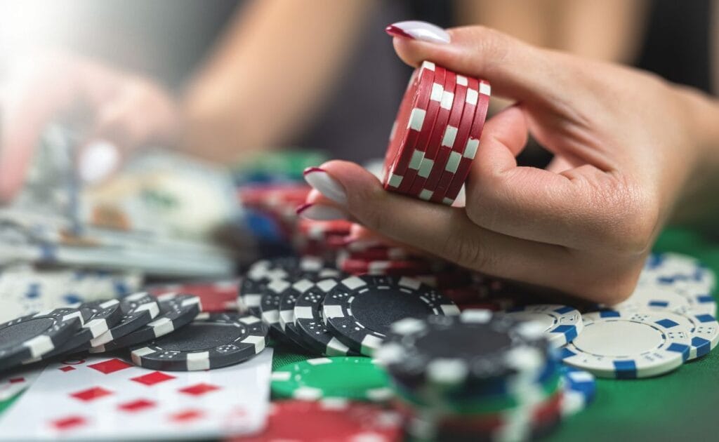 A person holding a small stack of red poker chips above a messy pile of poker chips on a poker table