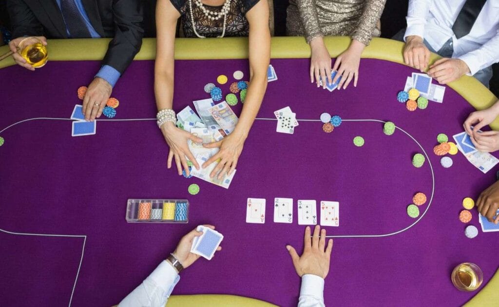 Top view of people playing poker gathered around a purple poker table in a casino, one person pulls a pile of money towards herself 