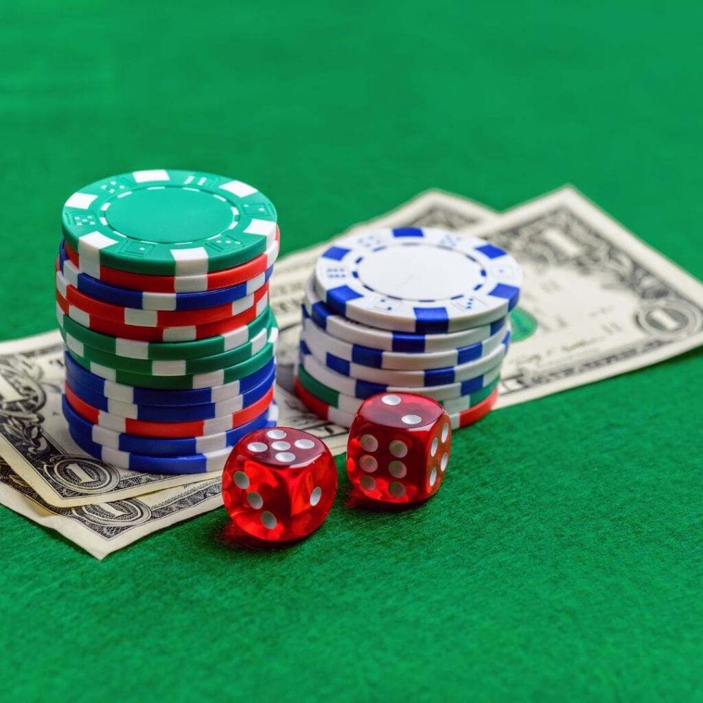 Two stacks of poker chips on two dollar notes next to two red six-sided dice on a green felt poker table