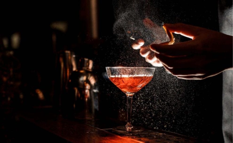 A barman pouring a cocktail, at a dimly lit bar.