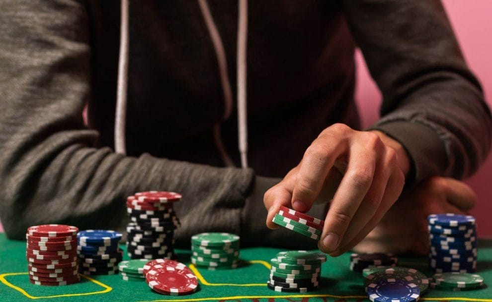 a person sitting a green felt poker table picking up from one of many poker chip stacks