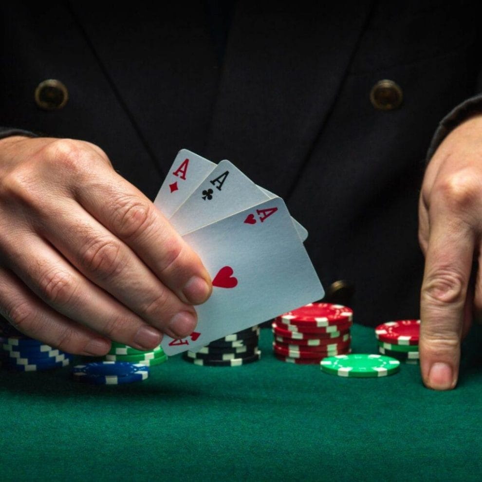 a person holding three of a kind ace playing cards above a green felt poker table with poker chips stacked on it