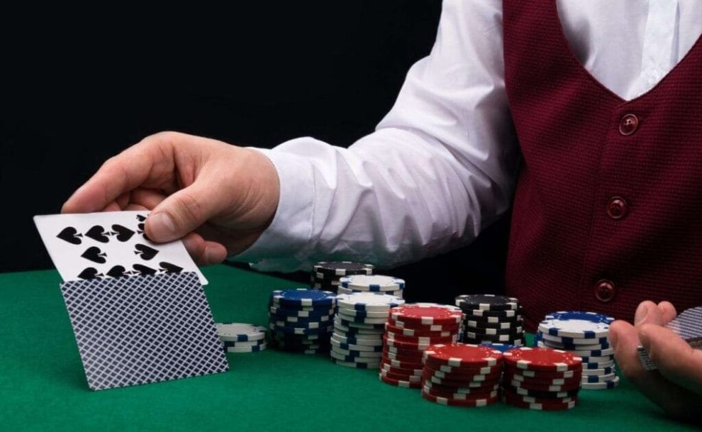 A closeup of a poker dealer reaching over the placed bets to flip a face-down playing card using another card.