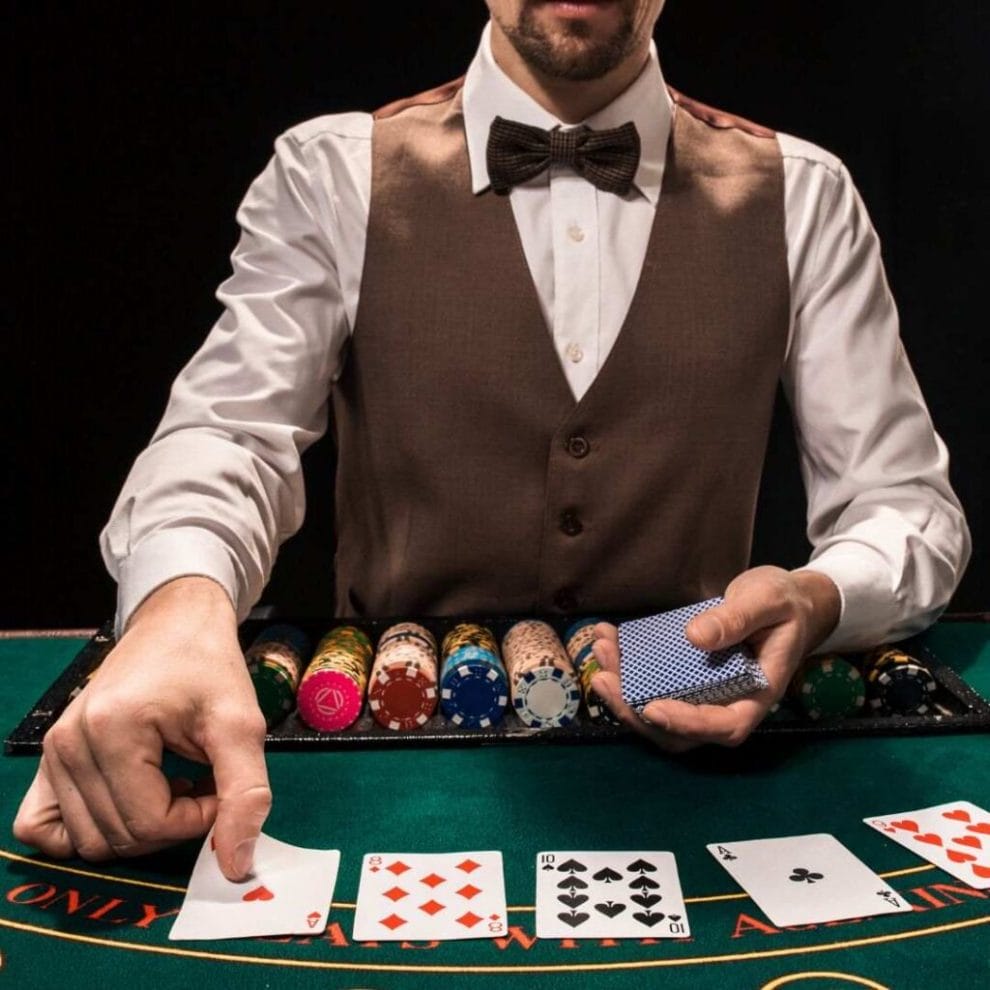 A shoulders-down view of a male poker dealer placing the community cards face up on a poker table.