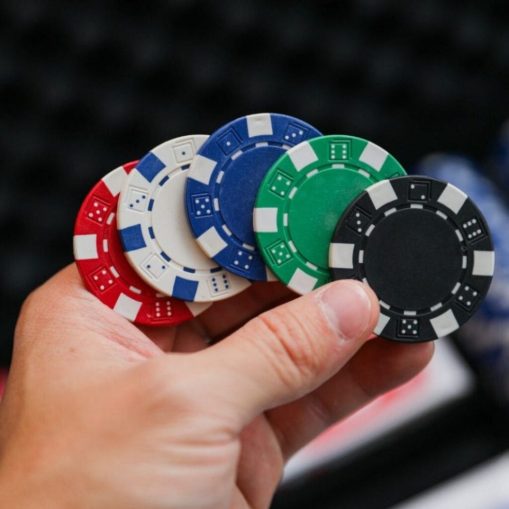 A closeup of a hand holding five fanned out poker chips of different colors.