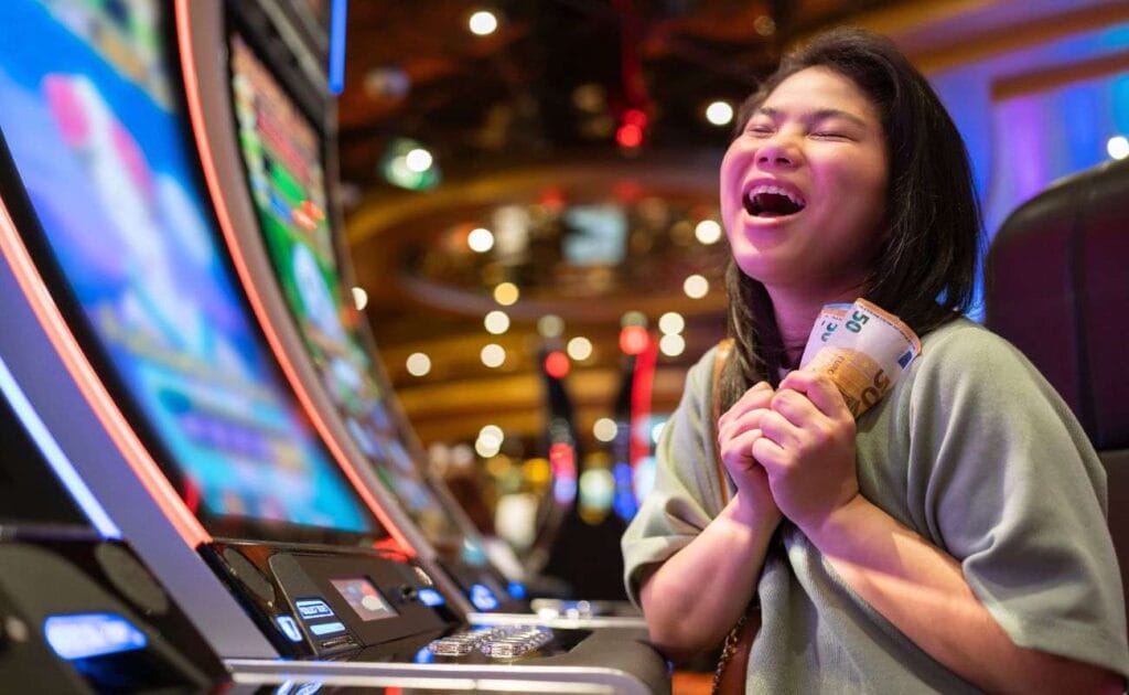 A very happy and excited woman smiling and clutching her winnings at a slot machine.