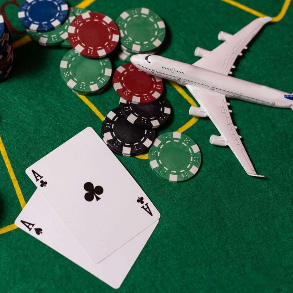 A pair of aces, scattered poker chips and a toy aeroplane on a green felt poker table.