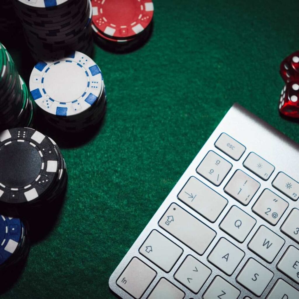 a computer keyboard on a green felt surface surrounded by poker chips and red dice