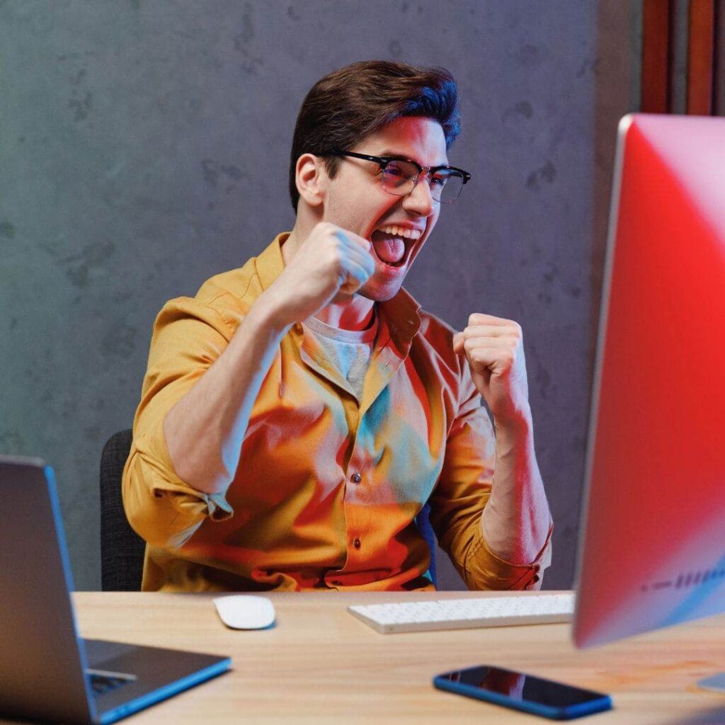 a man is cheering at his computer screen in excitement