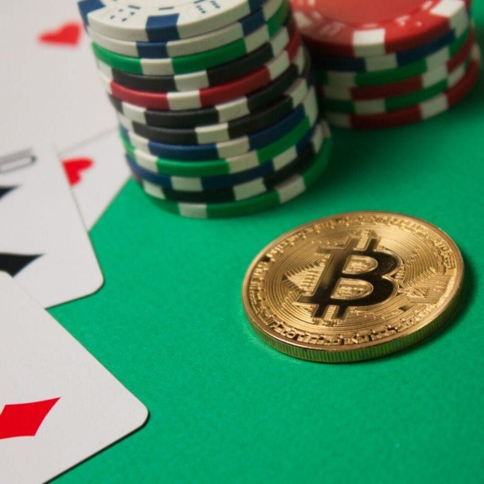 A stack of casino chips, some traditional playing cards, and a Bitcoin, arranged on a green felt poker table.