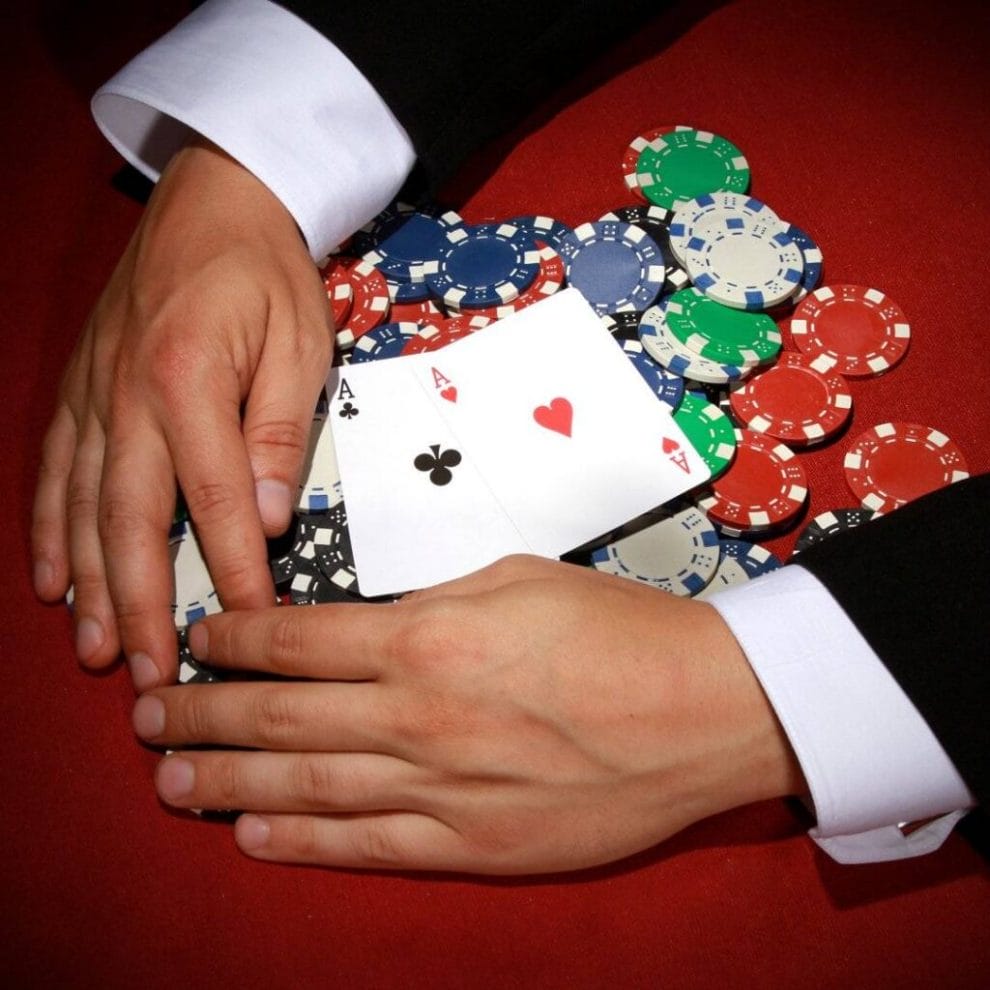 A poker player pulling poker chips with two aces on top towards themselves.