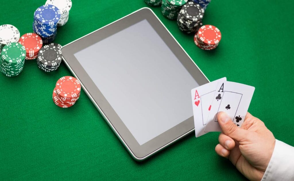 A hand holding playing cards with casino chips and a tablet device on a table.