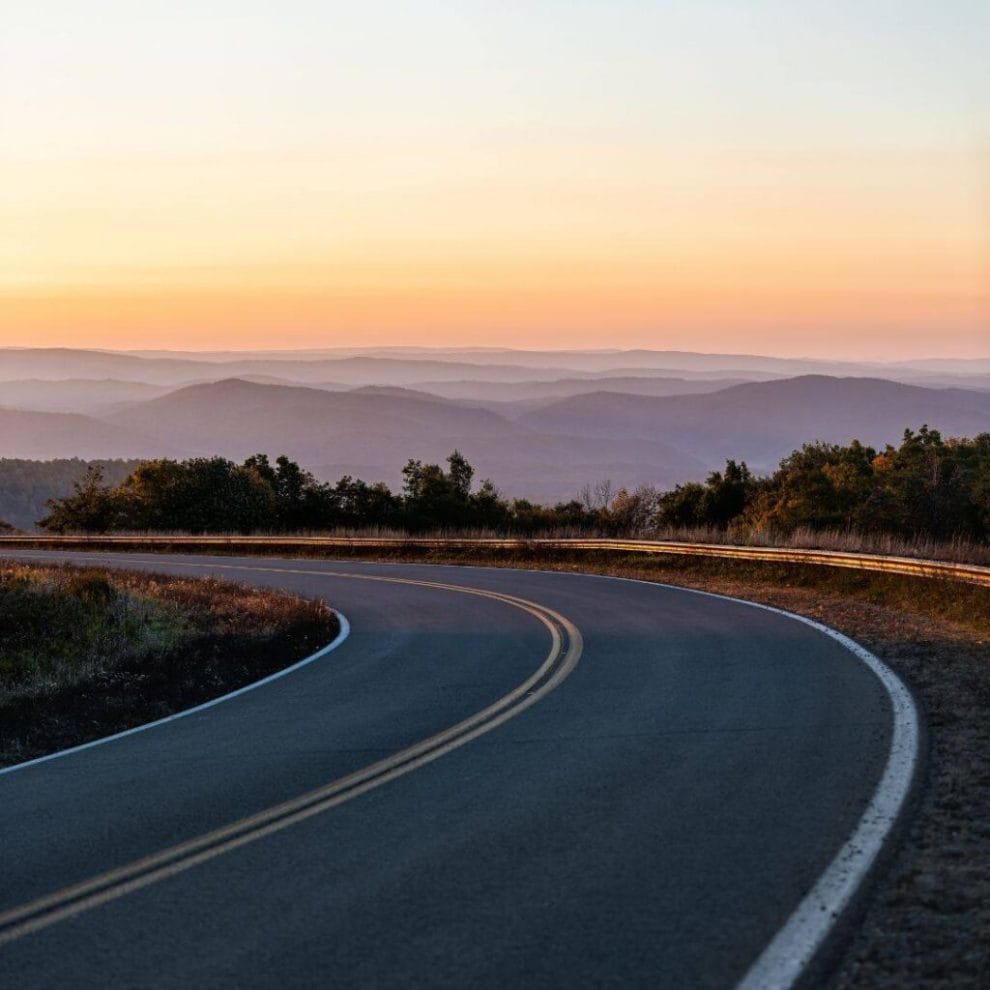 a winding road with mountain views in the background at sunset