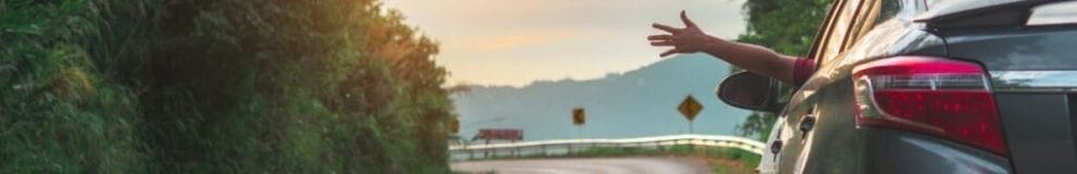 a person’s hand sticking out of the car window while driving on a windy road with views of mountains in front of the car