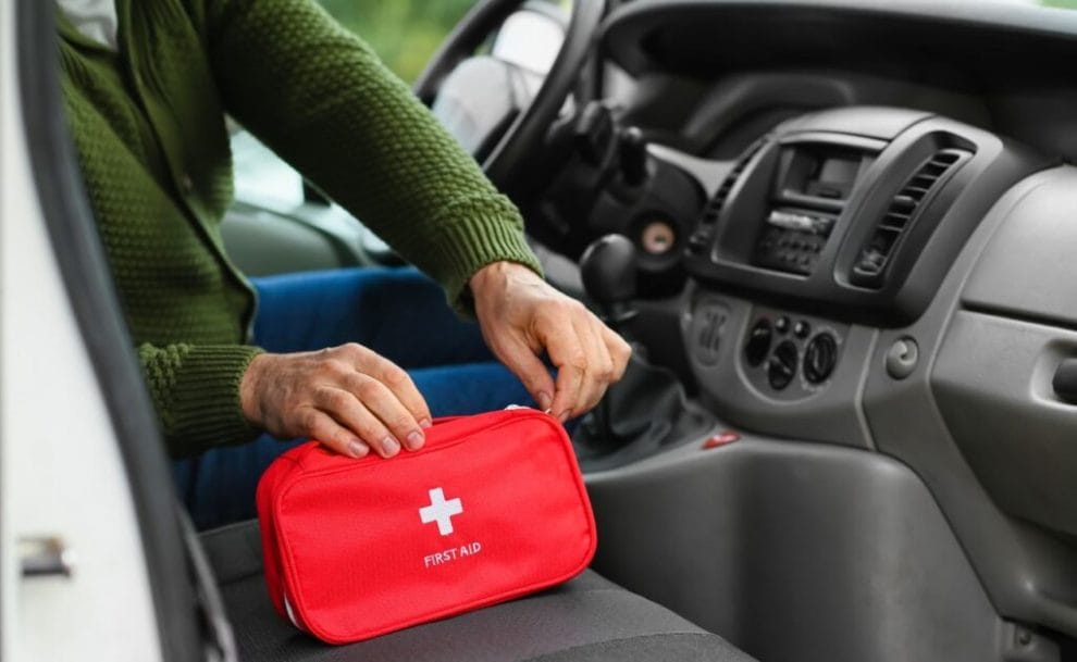 A person closes a red first aid kit in a car.