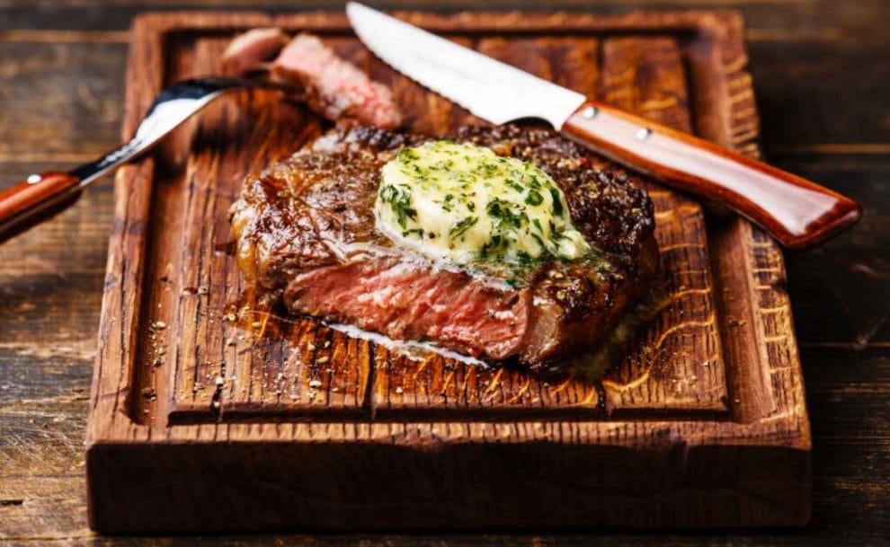 Ribeye steak with herb butter on a wooden board.
