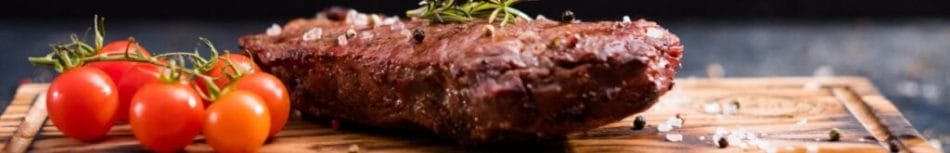 Steak and tomato on a wooden chopping board.