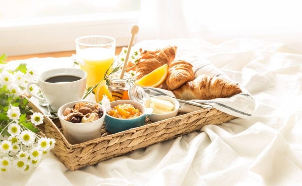 A gourmet breakfast tray sitting on a bed next to a bunch of flowers.