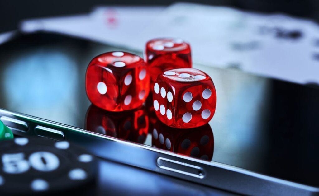 the focus is on three red six-sided dice on a cellphone with poker chips and playing cards blurred in the foreground and background