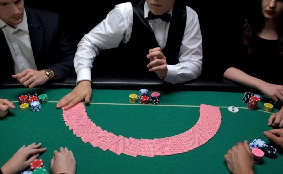 A card dealer spreads the deck of cards out face down on a poker table while shuffling them.