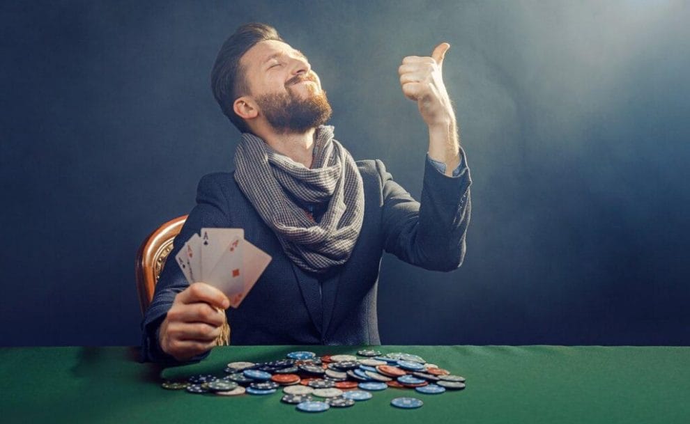 A poker player holds four aces and smiles while giving a thumbs up. They have a large pile of poker chips in front of themselves.