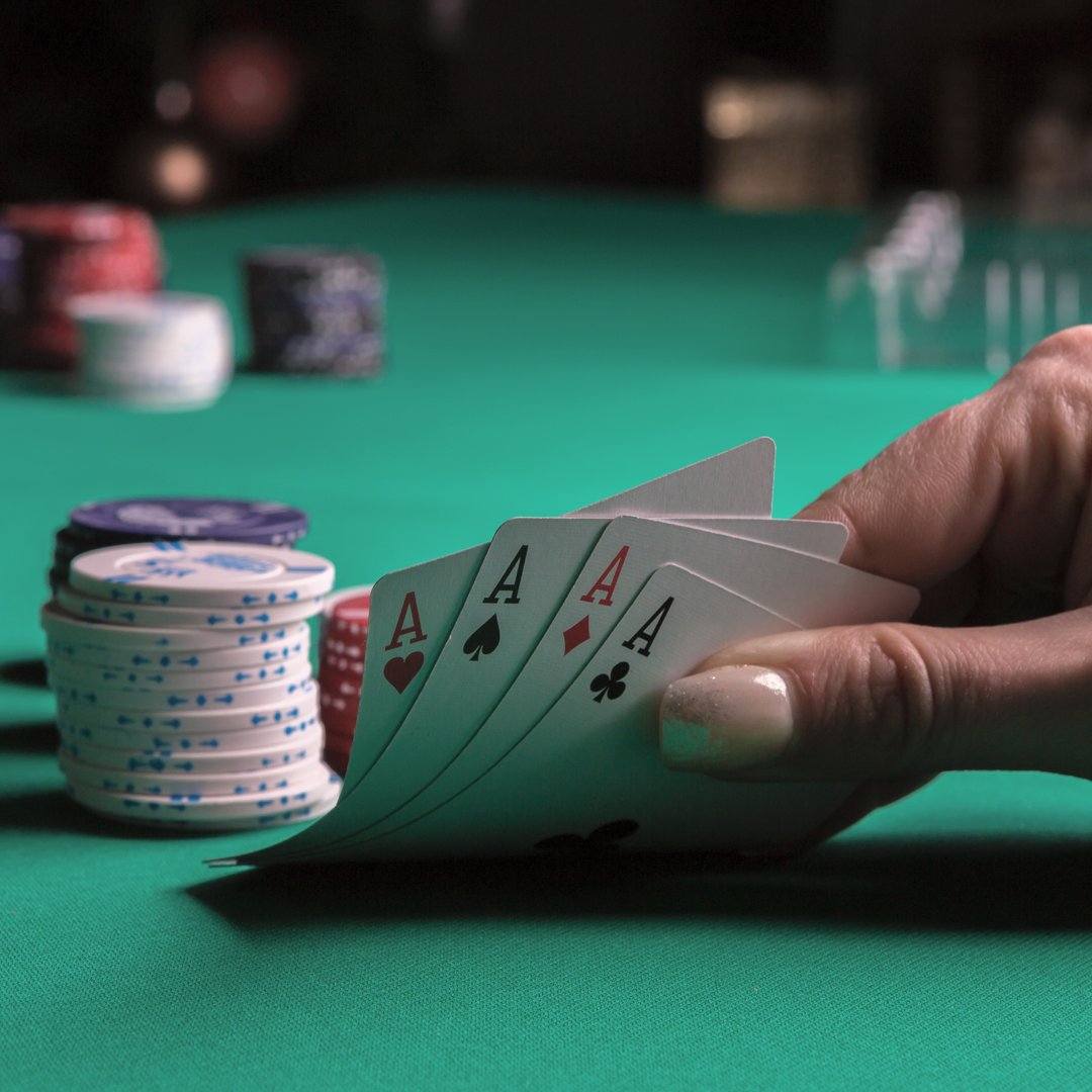 A poker player checks their four hole cards. They have four aces. There is a small stack of chips behind their hand.