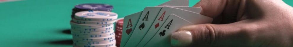 A poker player checks their four hole cards. They have four aces. There is a small stack of chips behind their hand.