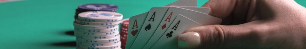A poker player checks their four hole cards. They have four aces. There is a small stack of chips behind their hand.
