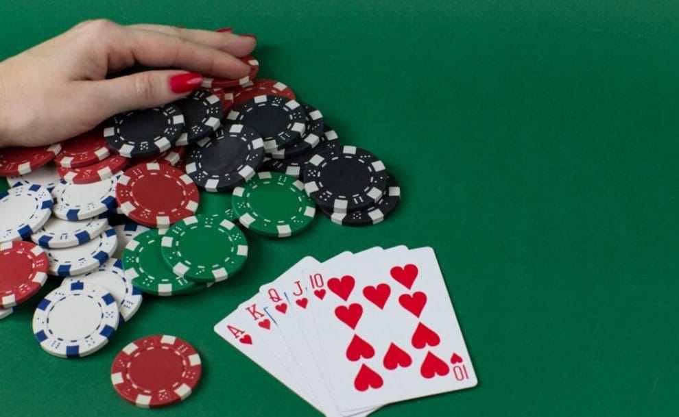 A poker player pulls a pile of poker chips towards themselves. There is a royal flush on the table in front of the pile of chips.