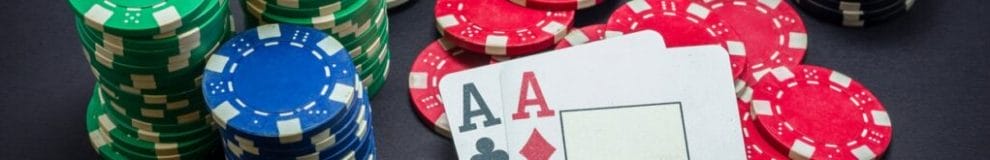 A pair of aces sit on a pile of red poker chips.