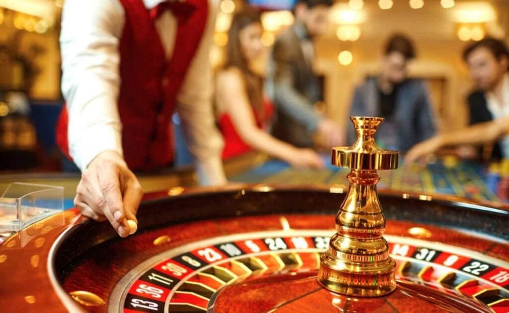 A casino croupier adding a ball to the roulette wheel.