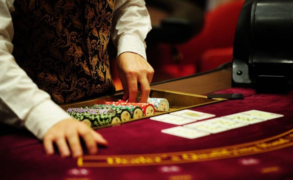 A casino dealer handling chips with playing cards laid out.