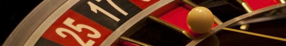 A close-up of a roulette wheel with a white ball in a red pocket.