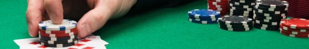 A man placing poker chips on playing cards on a green felt poker table with poker chips on it.