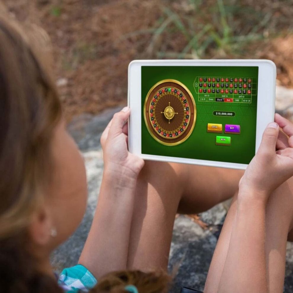 A woman plays online roulette on a tablet while sitting outside.